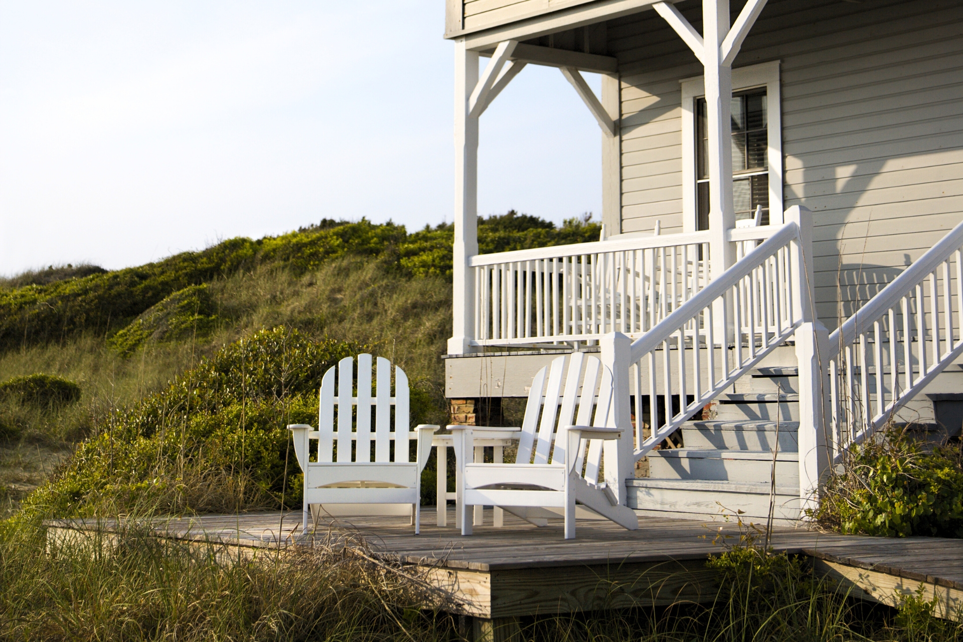 Coastal home porch with white chairs overlooking sand dunes, symbolizing peace of mind and lifestyle protection with umbrella insurance in Wilmington North Carolina