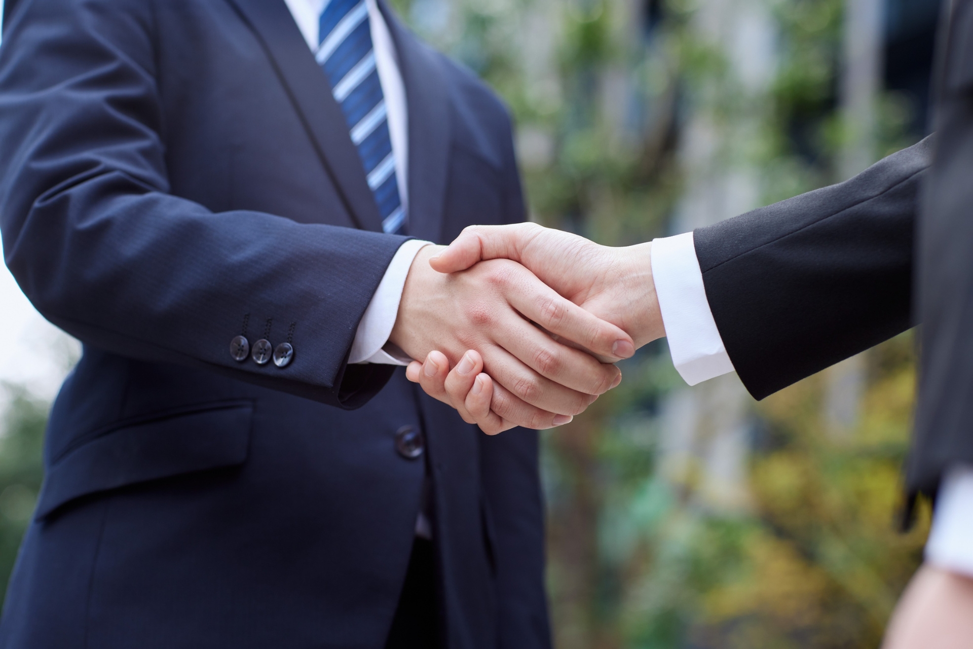 Two professionals in business suits shaking hands during a meeting.