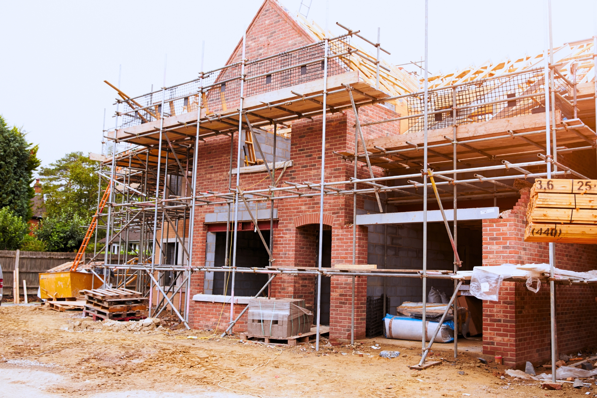 New brick home under construction with scaffolding, exposed framing, and building materials on site.