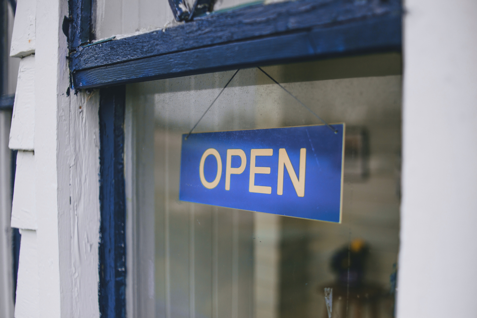 Blue “Open” sign hanging in a storefront window of a small business.