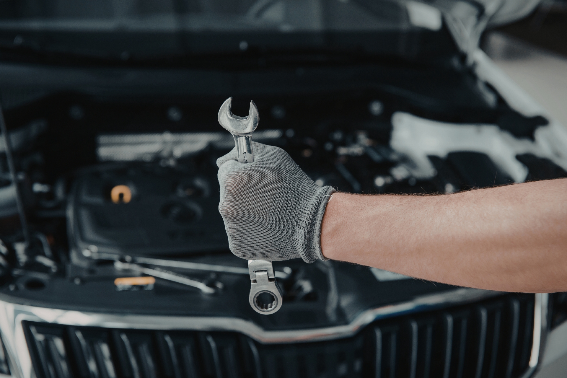 Mechanic holding a wrench in front of an open vehicle engine bay, representing garage liability insurance for auto repair and service businesses.