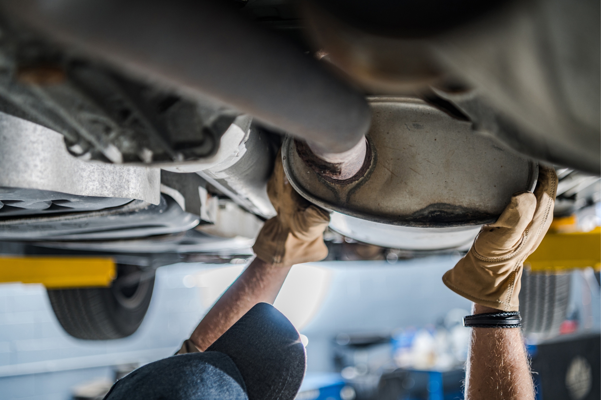 Mechanic performing exhaust repair under vehicle, replacing muffler and inspecting exhaust piping system