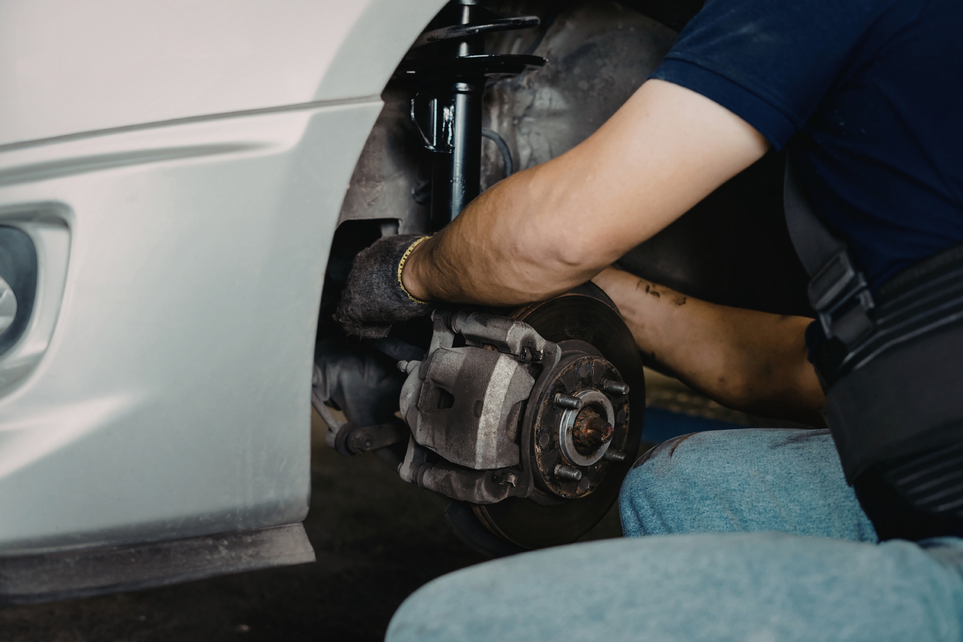 Mechanic repairing a vehicle’s front brake system with exposed rotor and caliper inside a garage.